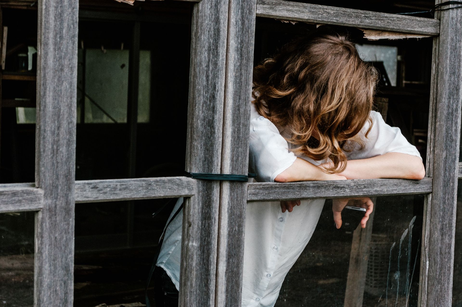 A woman hiding her face outside a broken window, struggling to figure out what is going on.  How can you tell if you are a worrier, nervous, or have anxiety? Magnolia Psychotherapy provides treatment for anxiety disorders and can help you manage these feelings.
