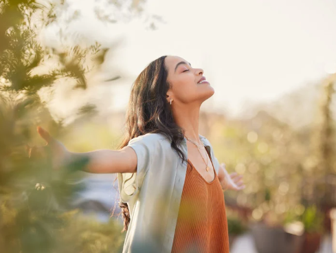 Woman holding out arms in nature feeling content and grateful