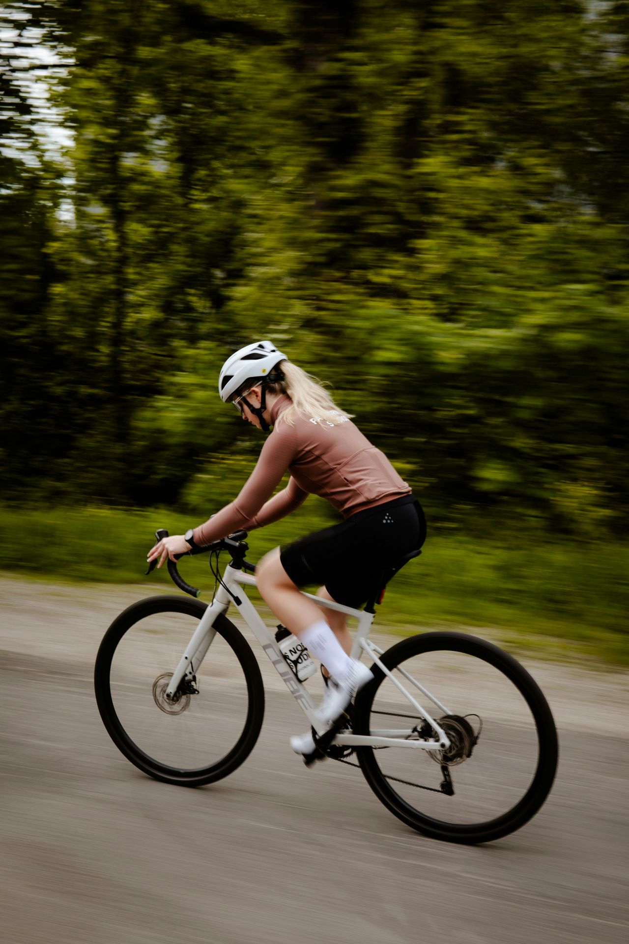 Woman cycling fast on a white road bike, looking polished and athletic — the picture of someone who has it all together