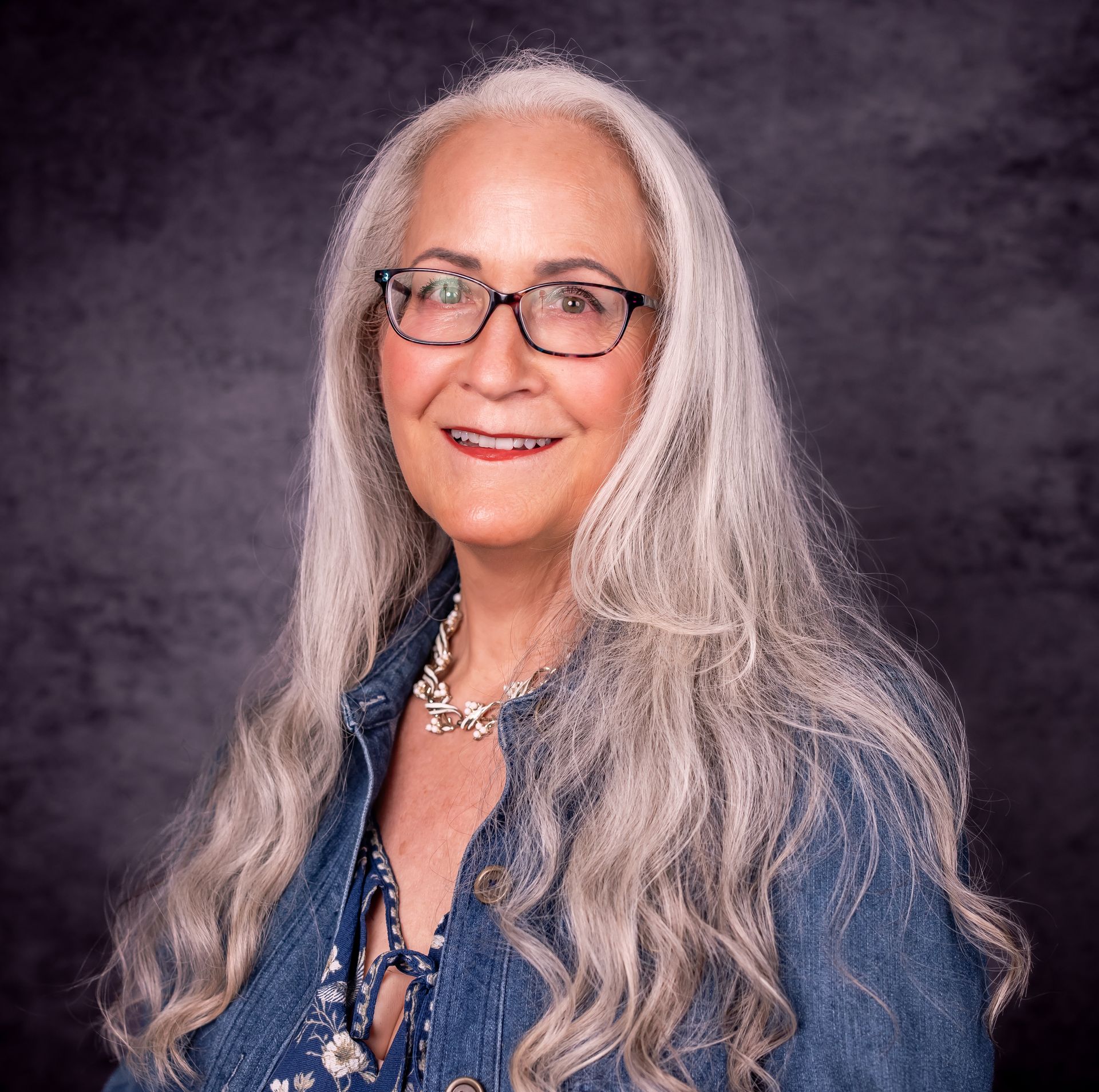 Text reading ‘Coping Skills for Parents of Neurodivergent Children: Creating Calm at Home’ appears alongside an image of Abby McCarrel, a warm and experienced psychotherapist with long silver hair and glasses, seated outdoors. The image represents parent counseling and online family therapy that helps parents of neurodivergent children learn coping skills to reduce overwhelm, regulate their nervous system, and create a calmer, more connected home environment.