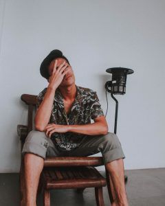 Hispanic young father with dark hair sits in a counseling session with his hand over his face feeling guilty about mental illness.