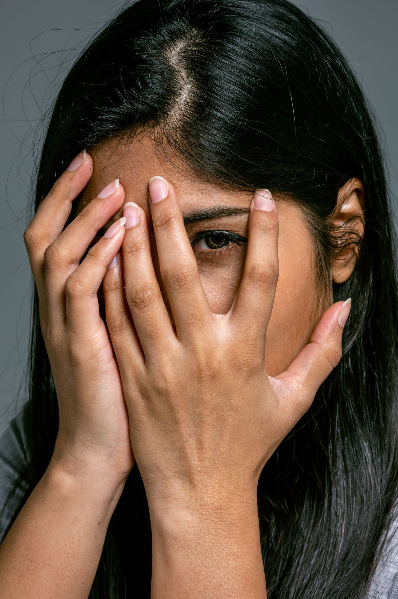 Anxious young woman peering through covering hands
