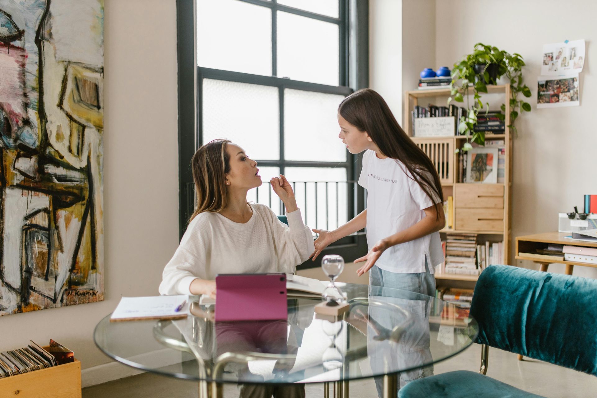 A mother is sitting at a glass table with a tablet and old fashioned, sand timer, talking to her daughter about treatment for ADHD therapist near me.