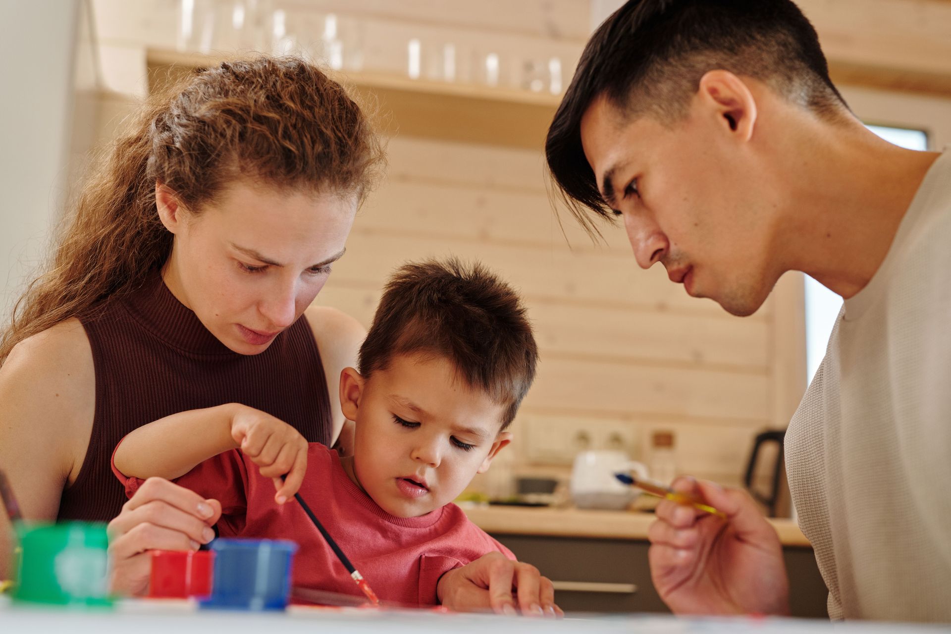 Mom and dad guiding their young son through a painting activity at home, reflecting the connection families rebuild through family therapy for neurodivergent kids in California.