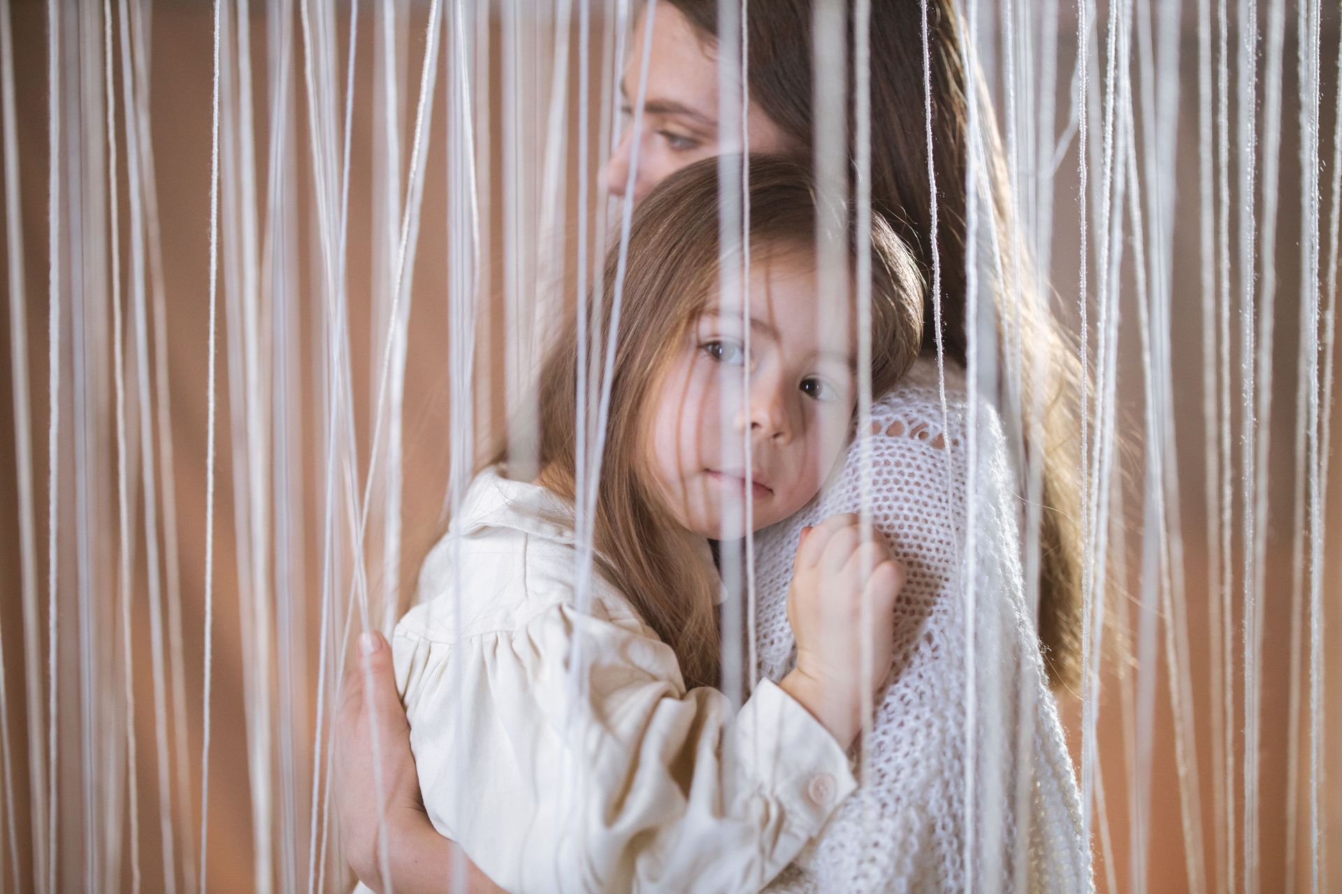 A young child with a sad, distant expression clings to her mother, illustrating child depression and emotional withdrawal — Welcome Home Family Therapy, California.