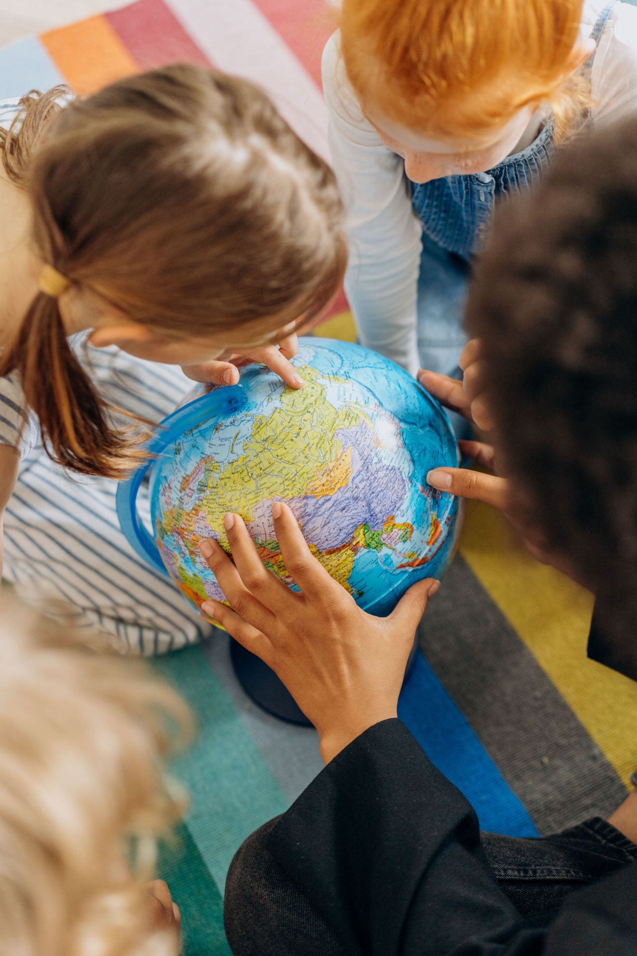 Children and a parent gathered around a world globe on a colorful rug, talking about scary news, parent therapy in California