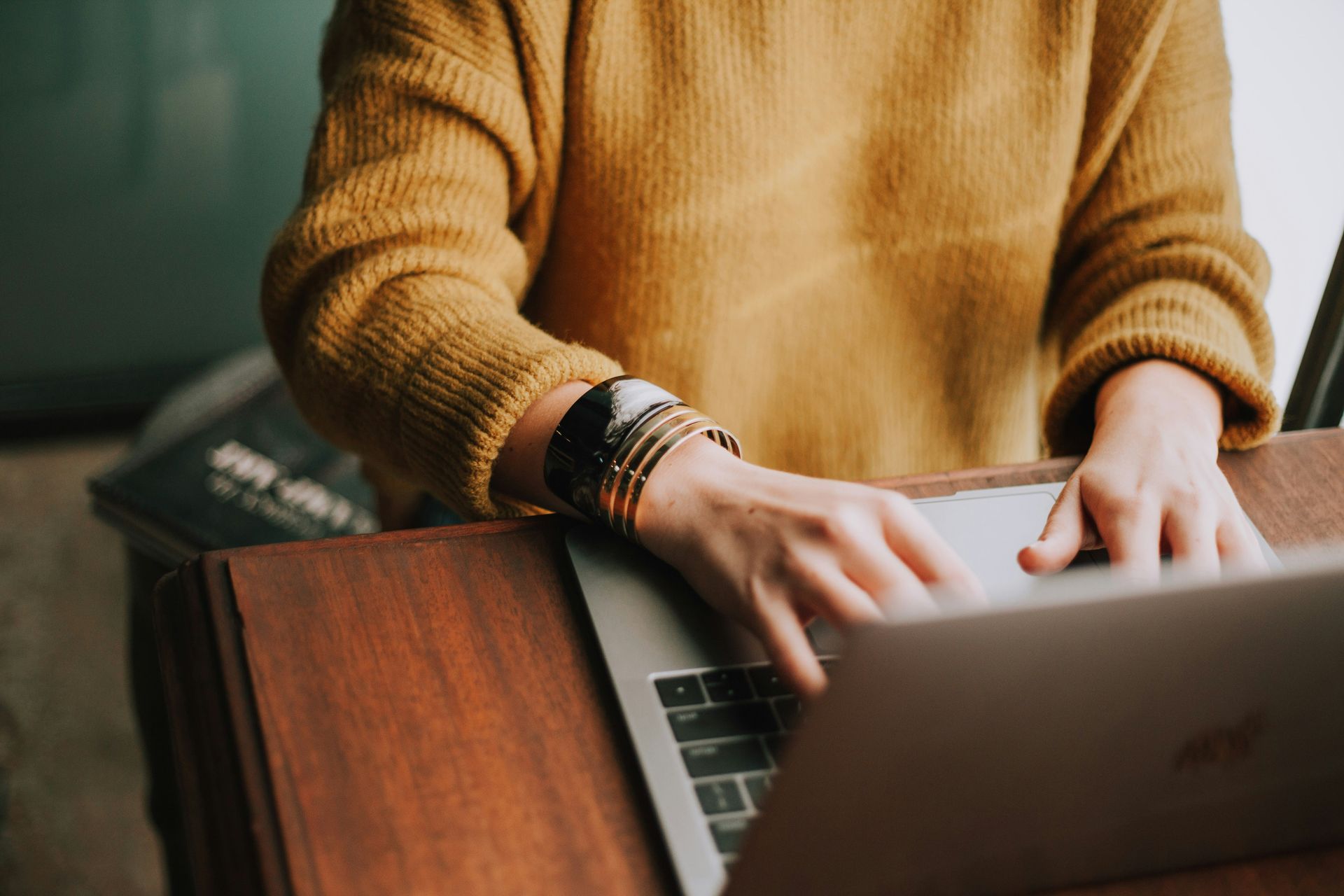 person in a mustard colored sweater typing on a laptop. 5 Things to Consider When Searching for a New Therapist. Online virtual counseling services