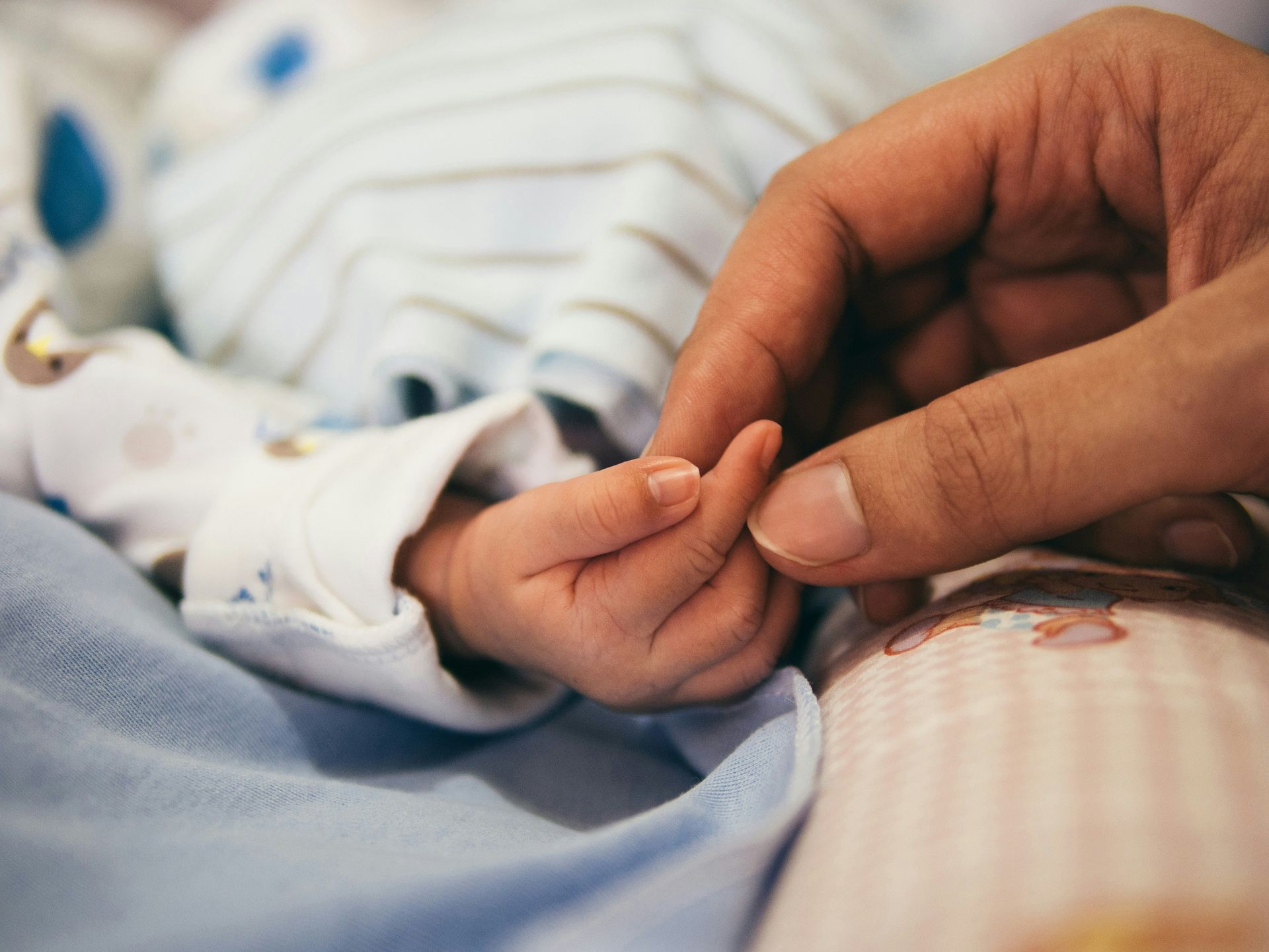 adult / parent/ caregiver hand holding the hand of an infant. Parents of dependent children are at an increased risk of stress and sleep impairment.
