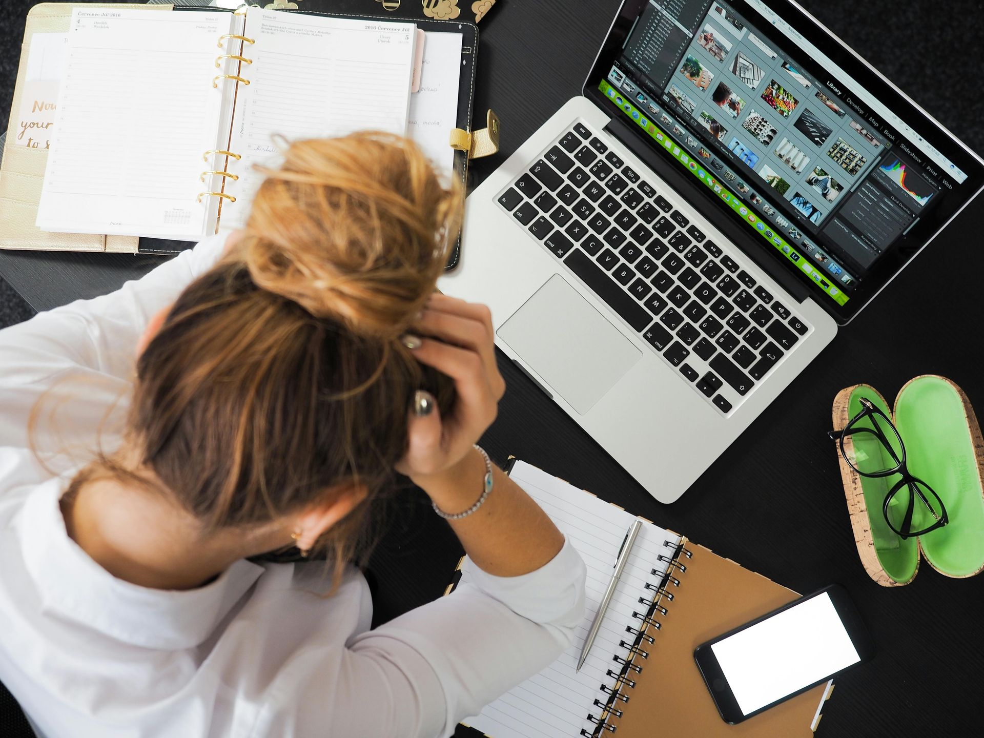 woman resting her head on her hands on a desk, visible is a laptop, and open notebooks. 45 regulation activities to boost well-being