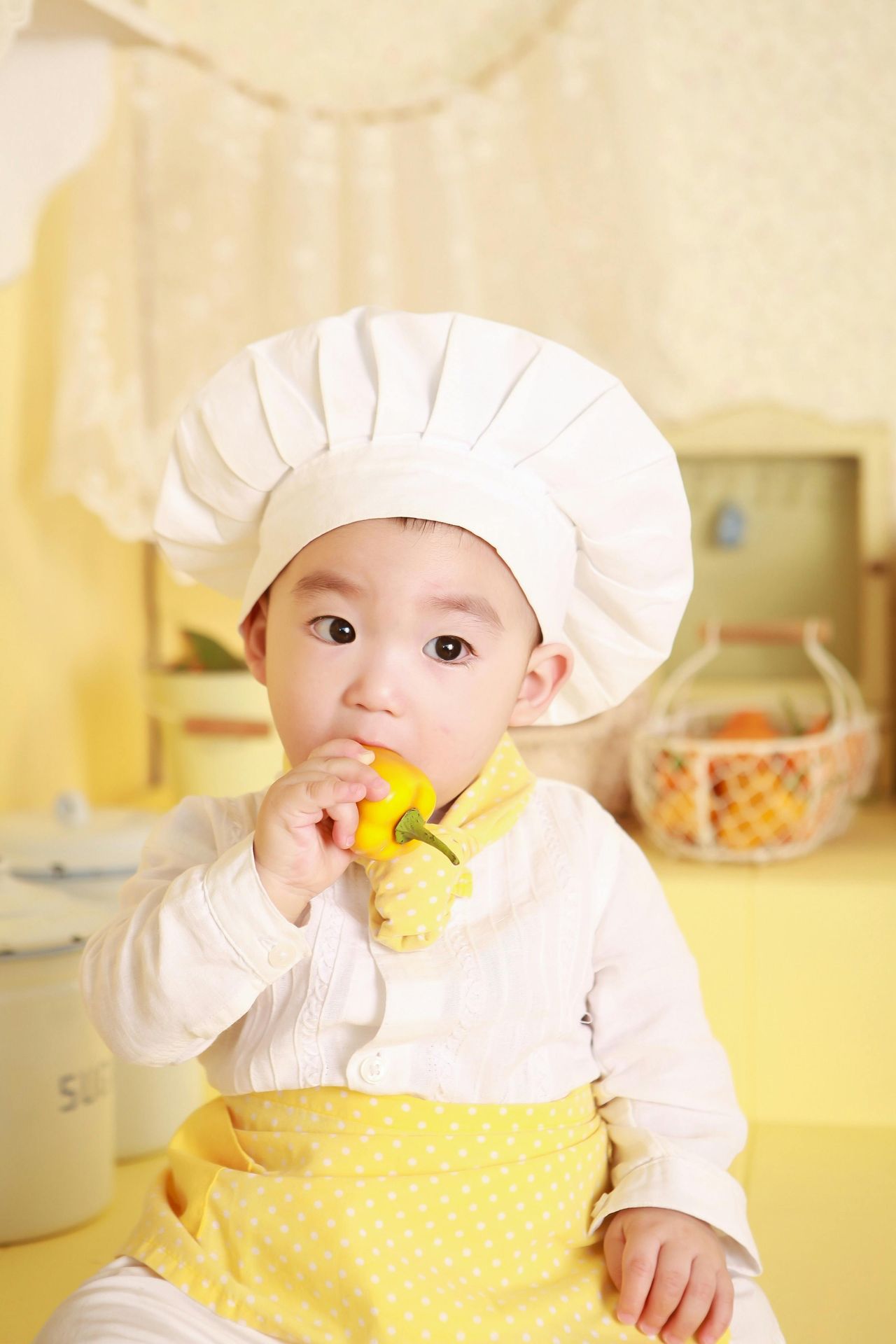 Asian baby in a chef hat and shift; holding a yellow pepper in his mouth (very cute). 45 activities to boost well-being