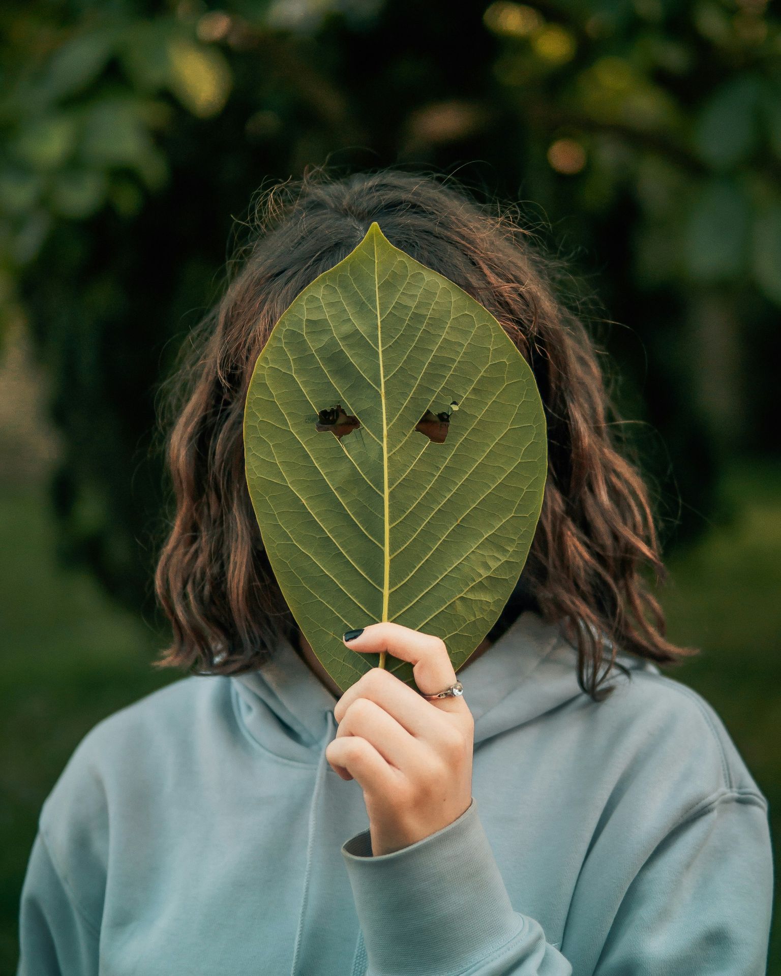 woman holding a leaf covering her face with eye holes cut out