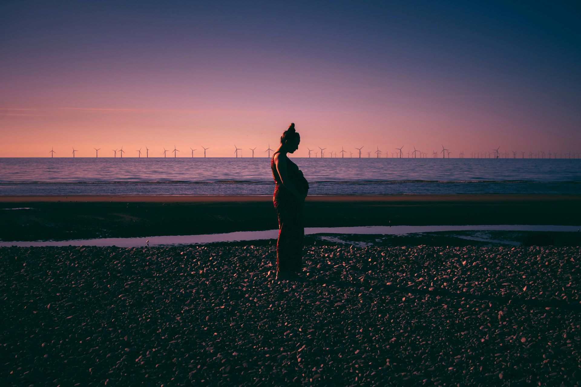 pregnant woman standing on a beach during sunset holding her baby bump. perinatal and postpartum depression anxiety OCD PTSD counseling Alaska online .