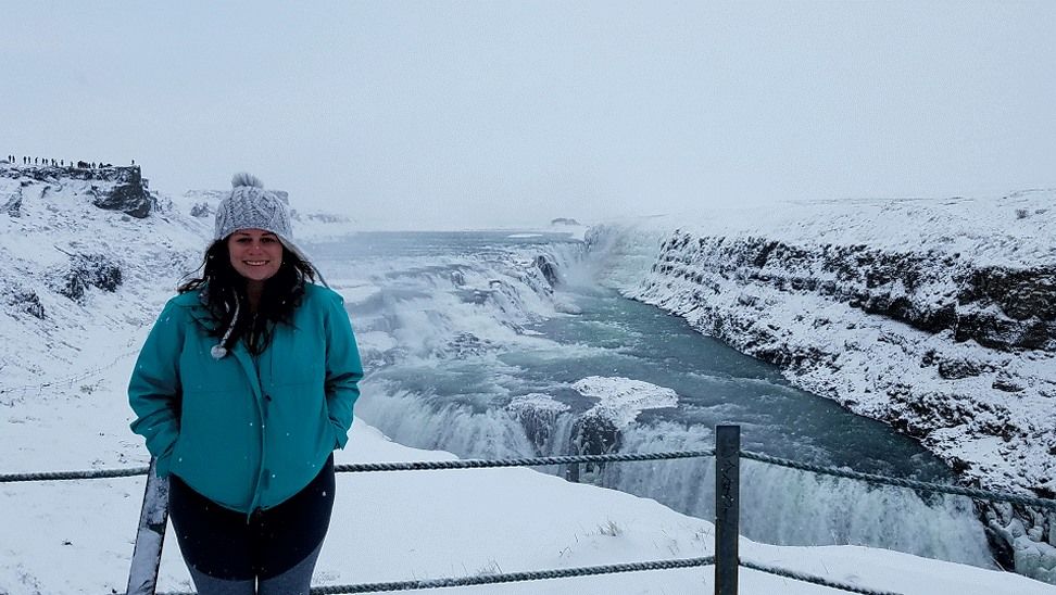 Nicole, a white woman wearing a green jacket, standing in front of a waterfall in Iceland during winter. Online therapist Alaska. Self-regulation activities for adults blog post