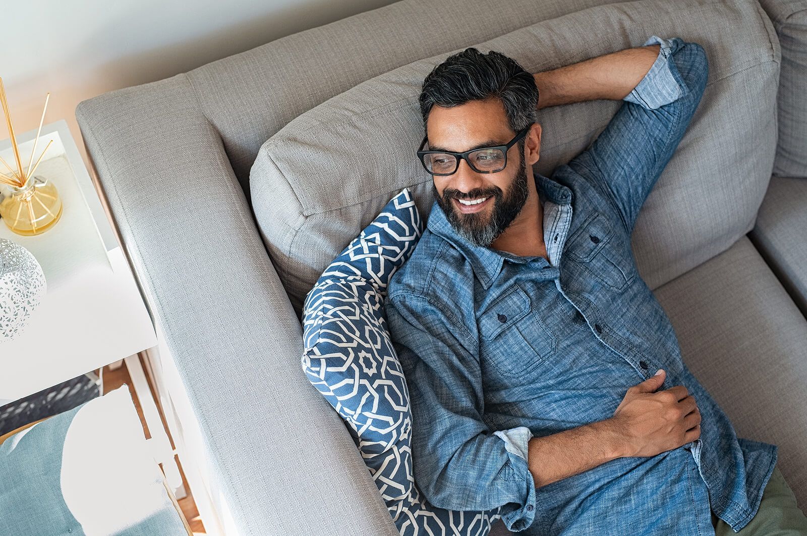 A man wearing glasses relaxing on a grey couch | men's therapist san francisco, ca | men's therapy san francisco, ca | online men's issues counseling california | 94609 | 94061 | 94941