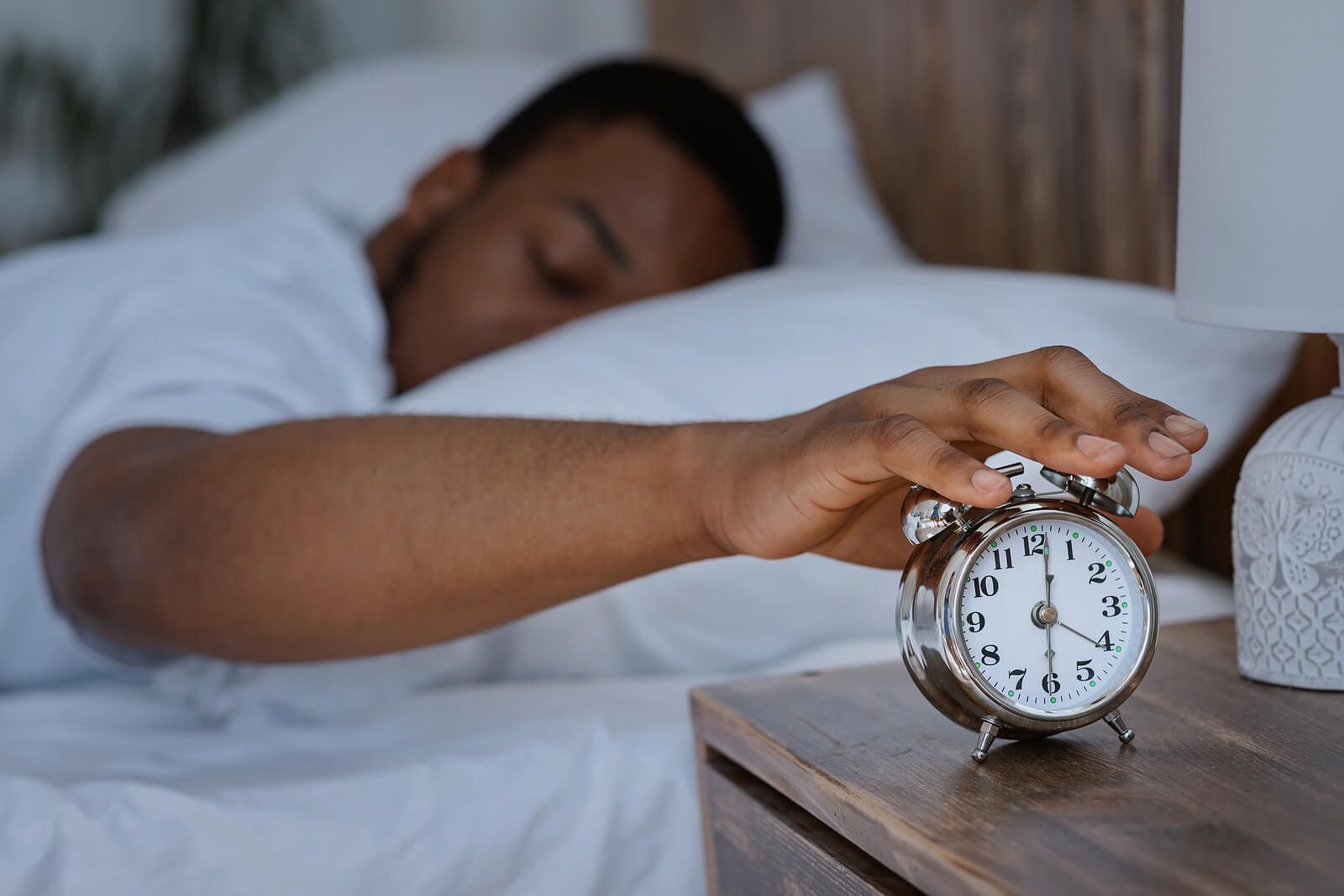 A black man sleeping reaching for his alarm clock | grief counselor san francisco | loss and grief treatment san francisco | therapist for grief san francisco | 94539 | 94110 | 94112