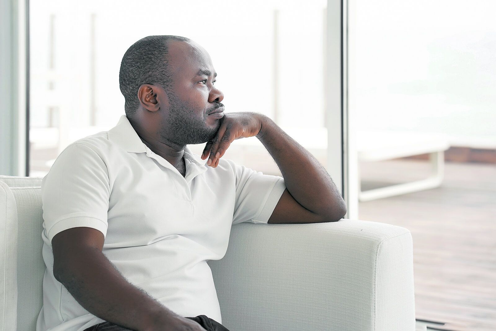 A man sitting on a white couch with his head resting on his chin | men's therapist san francisco, ca | men's therapy san francisco, ca | men's issues therapy san francisco, ca | 94608 | 94609 | 94061