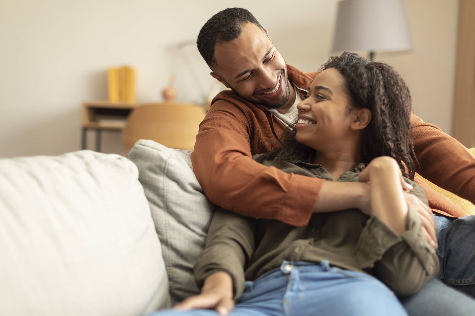 A couple cuddling together on the couch & smiling | men's therapist san francisco, ca | men's therapy san francisco, ca | online men's issues counseling california | 94609 | 94061 | 94941