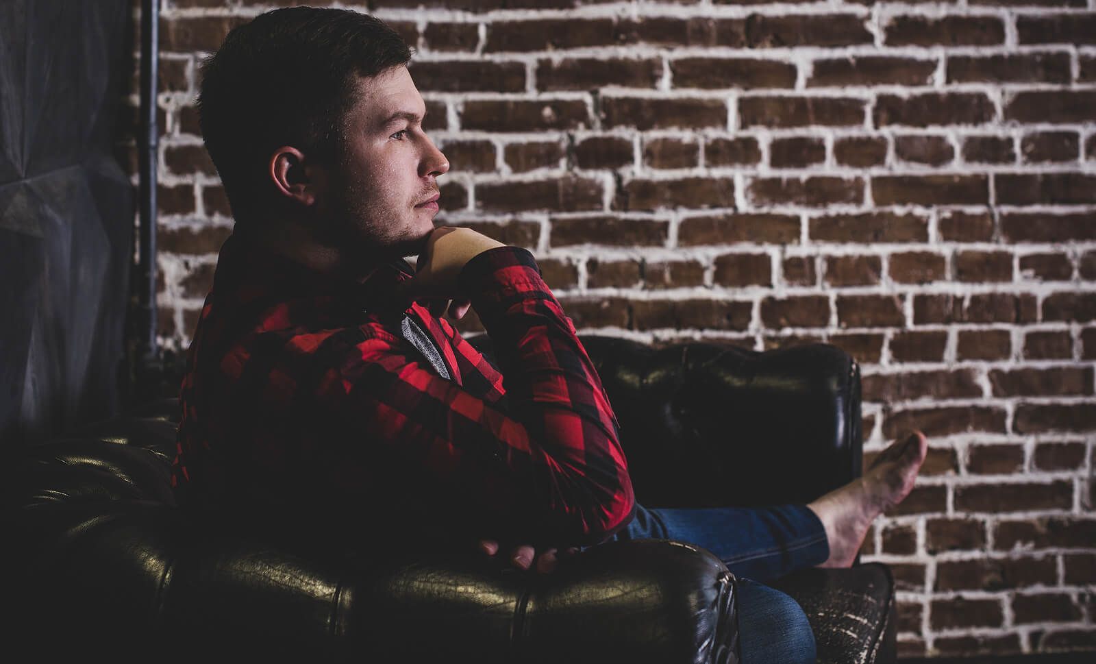 A man wearing a red flannel rubbing his chin while sitting on a couch | grief therapy in san francisco, ca | grief therapist san Francisco, ca | grief counseling san francisco, ca | 94122 | 94539 | 94110
