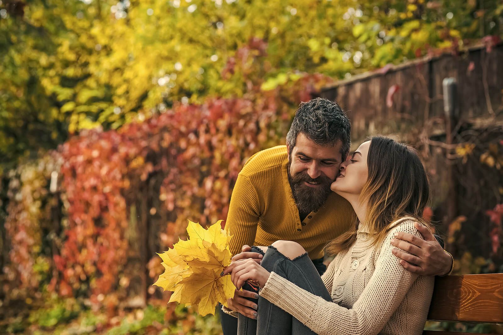 A woman kissing her partner on the cheek while holding yellow leaves | men's therapist san francisco, ca | men's therapy san francisco, ca | men's issues therapy san francisco, ca | 94608 | 94609 | 94061