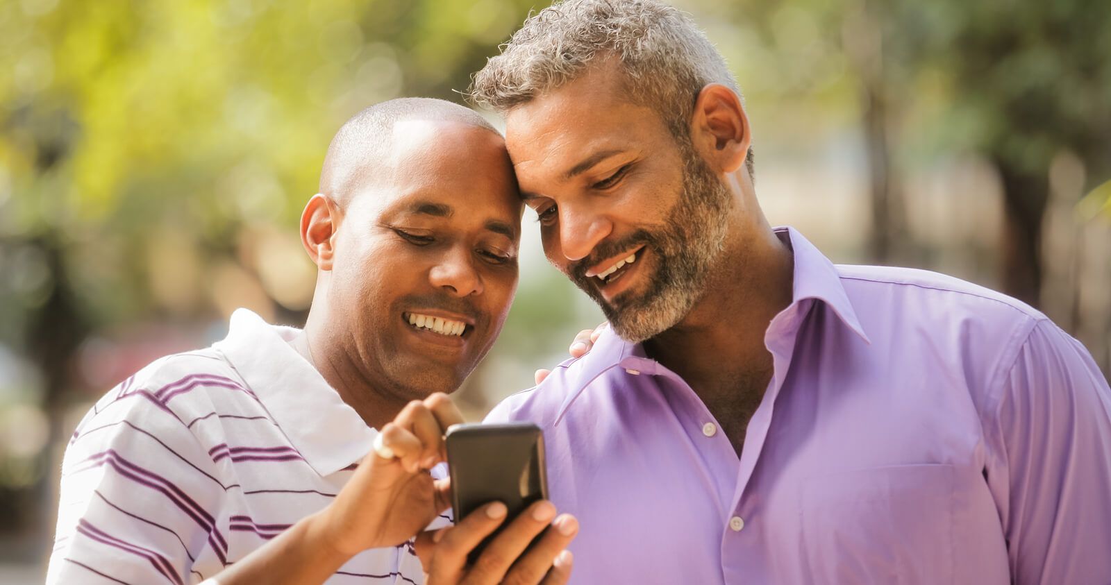 Two men smiling & looking at a phone together | counseling for men san francisco | men's therapy san francisco, ca | men's therapist san francisco, ca | 94607 | 94608 | 94609