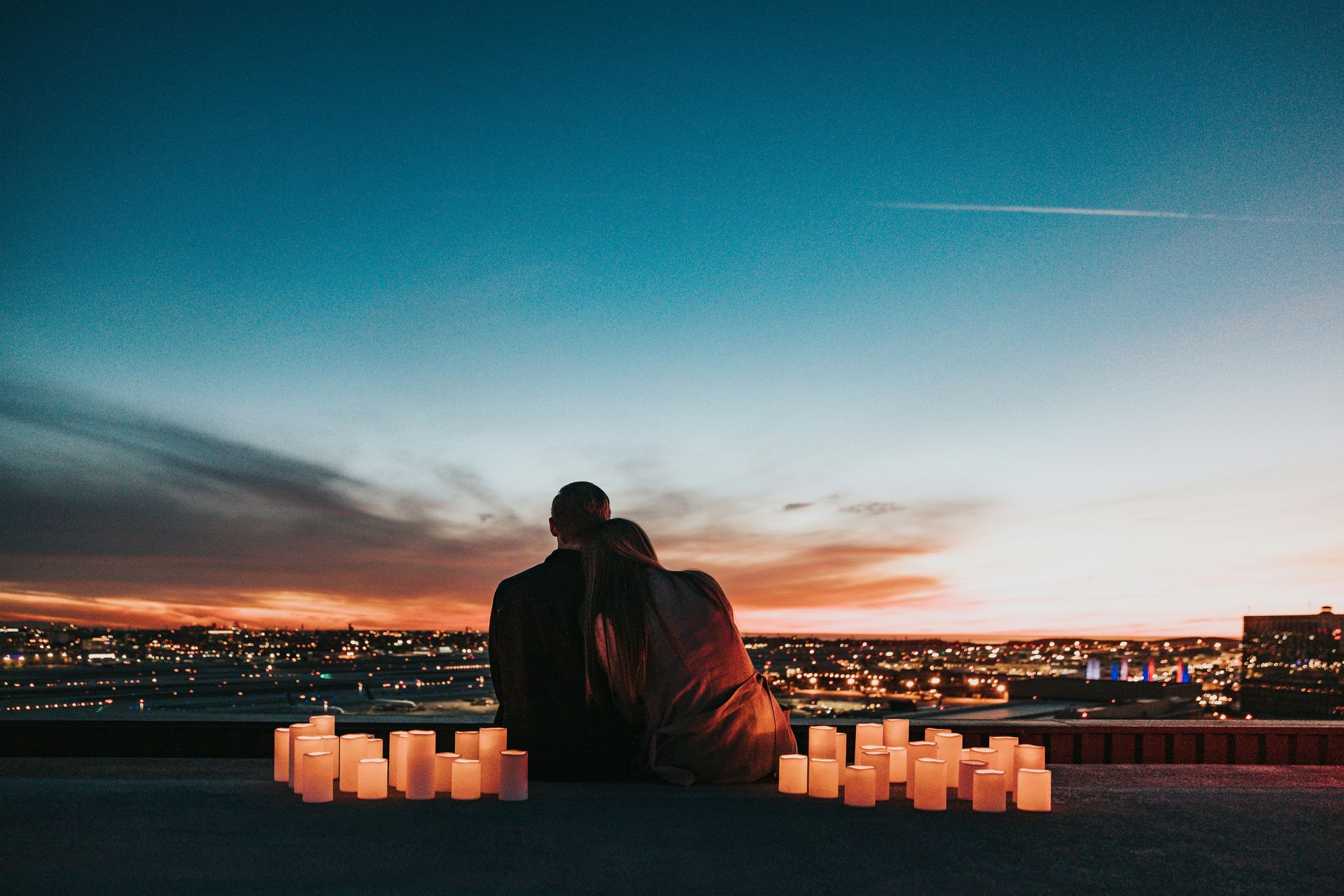 a view from behind a couple sitting looking at a sunset surrounded by lit-up paper-bag lanterns