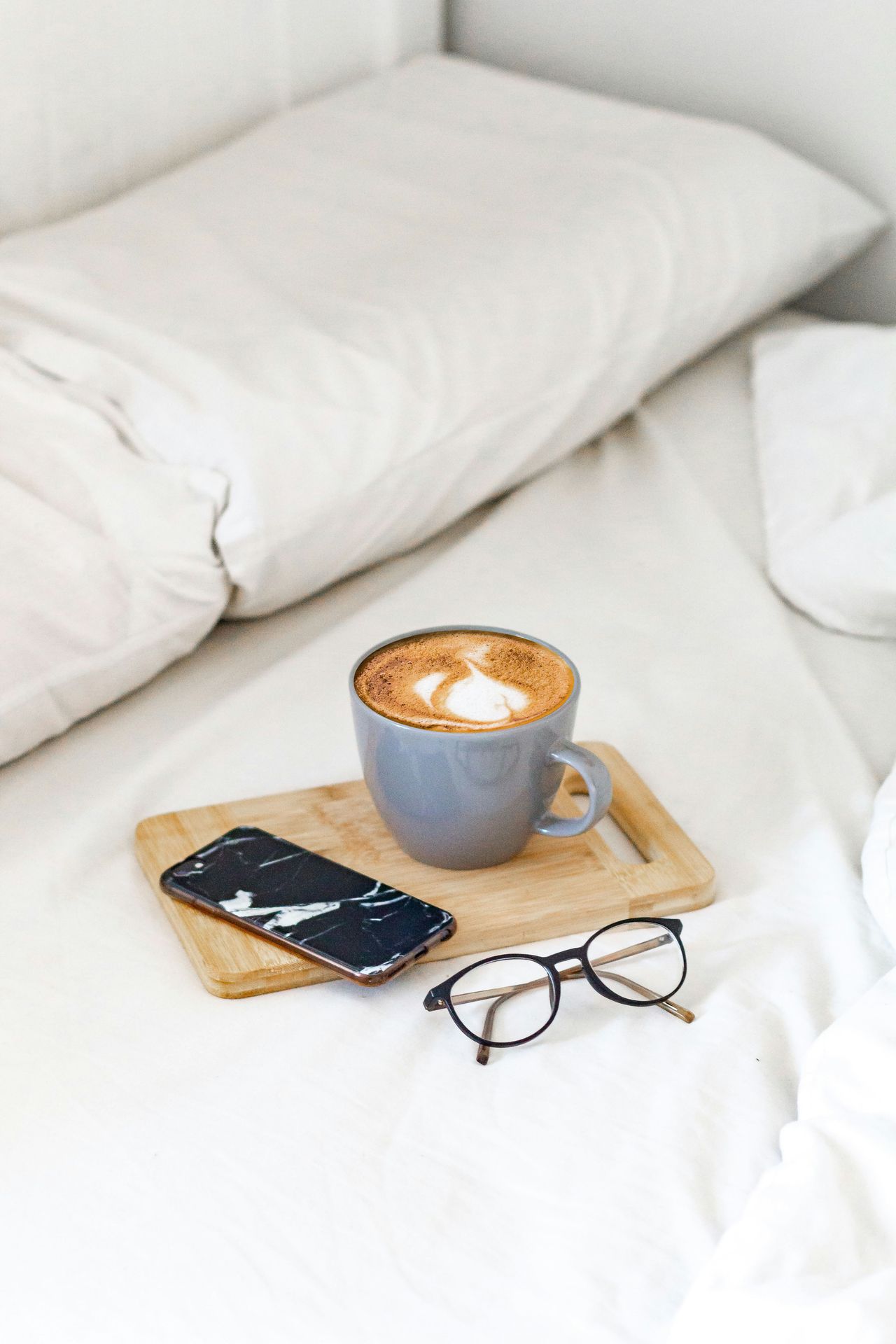a cup of coffee, pair of glasses and a cell phone sitting on a soft comfy surface like a bed