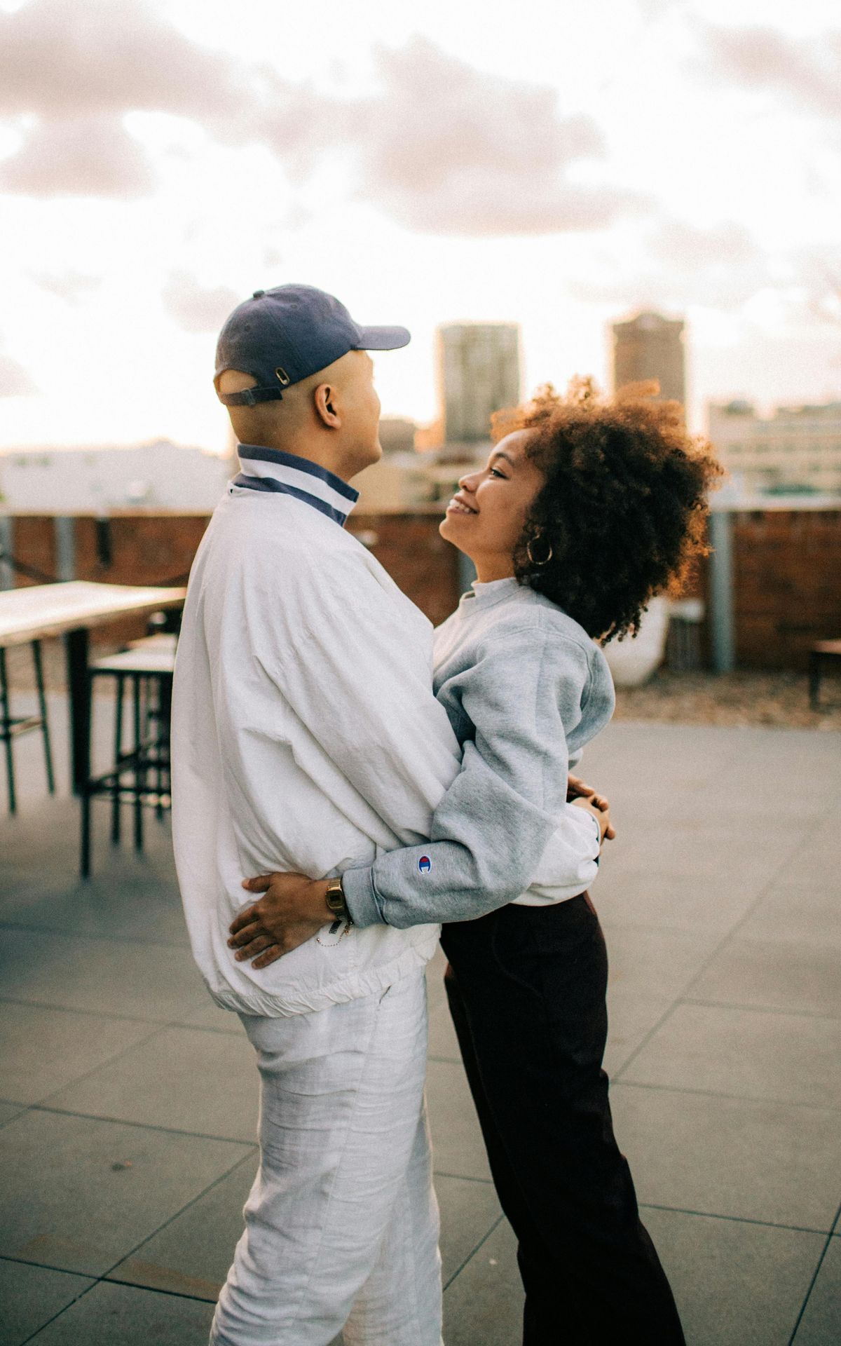 a cis-gendered black couples hugging on top of a building overlooking a city skyline, they are smiling and seem connected 