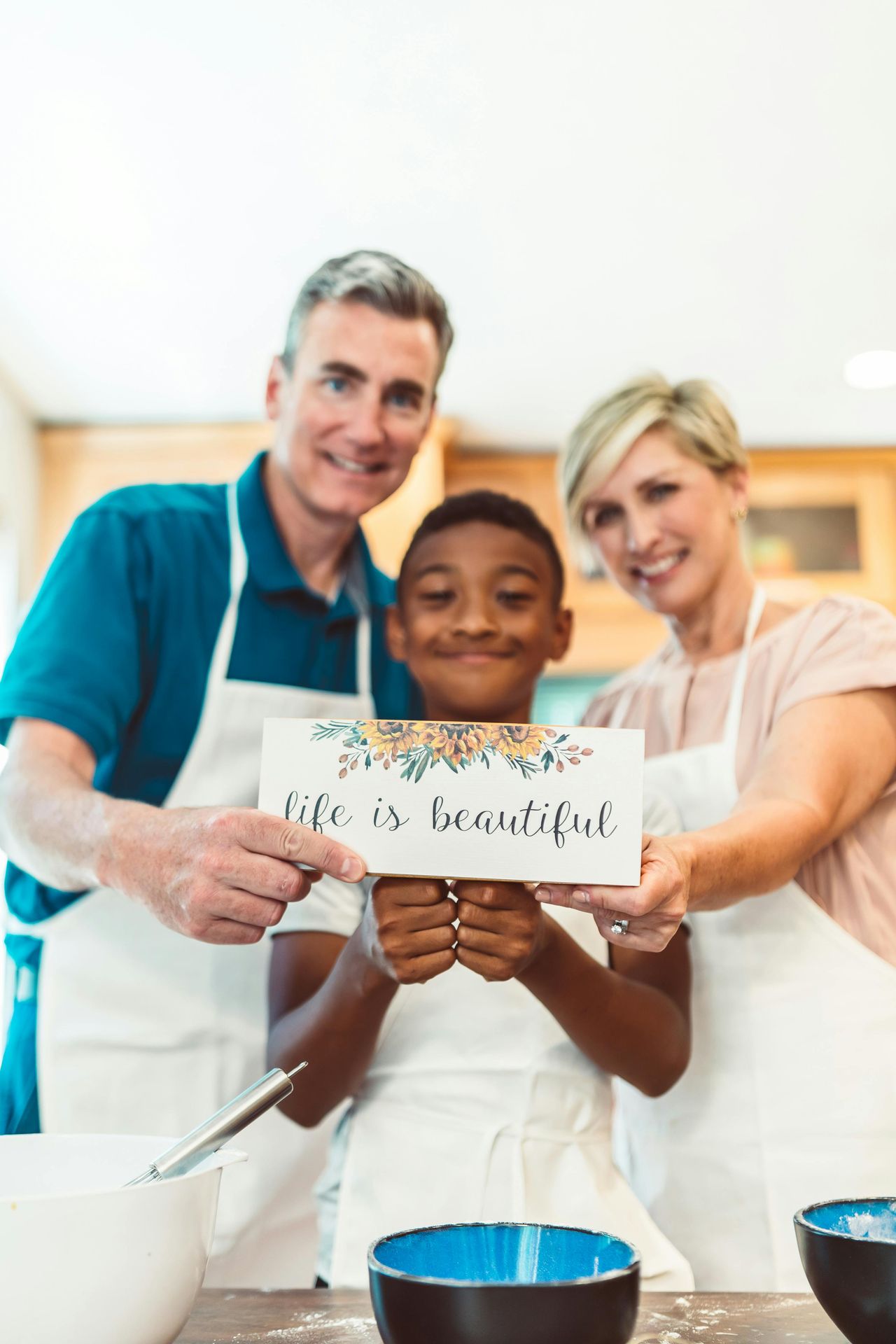 3 person-mixed cultural family all smiling and holding a sign that says "life is beautiful"