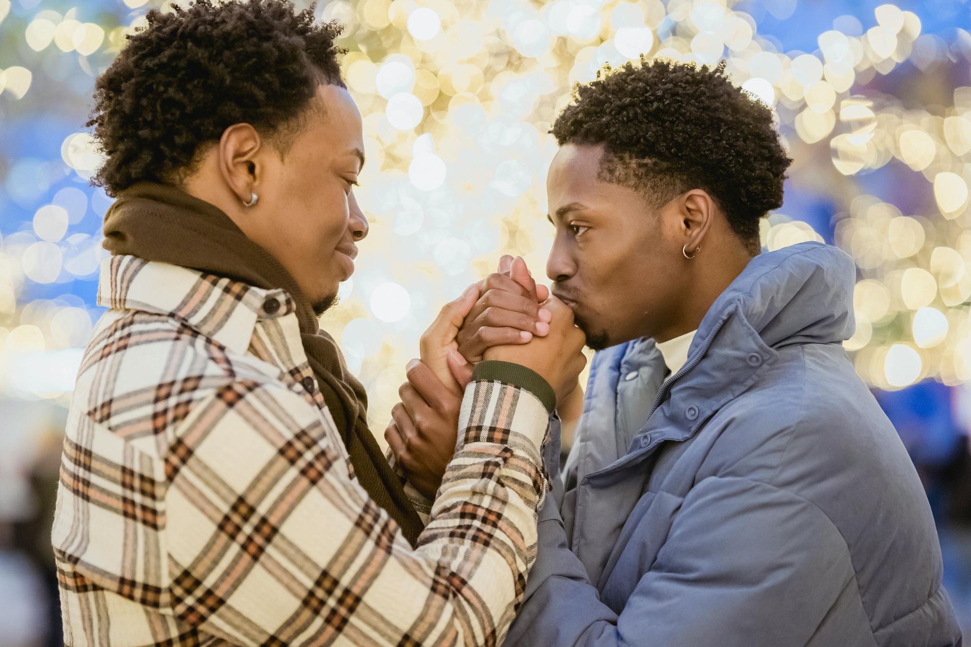 gay black couple in front of Christmas lights one is holding and kissing the other's hand, Uplift and Connect Counseling, Katheryn Barton