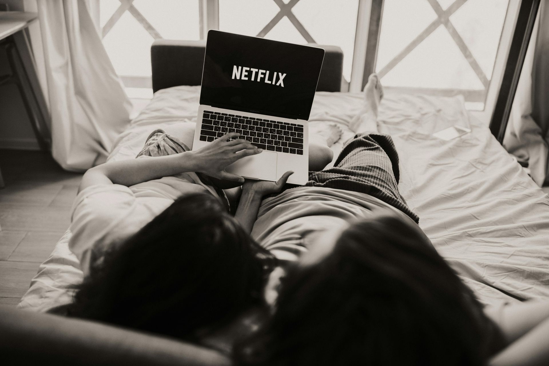 a black and white photo of a couple lying in bed looking at a computer screen that says netflix