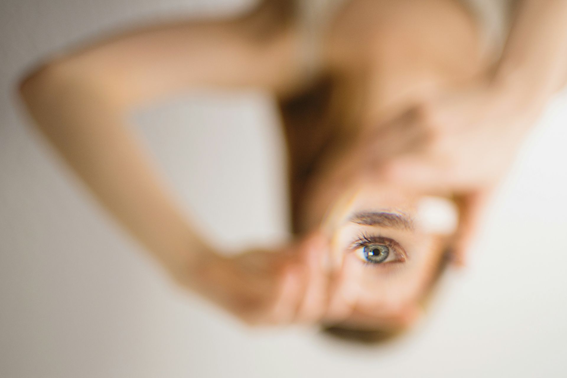 a cryptic photo of a woman holding a small mirror where she can only see one eye