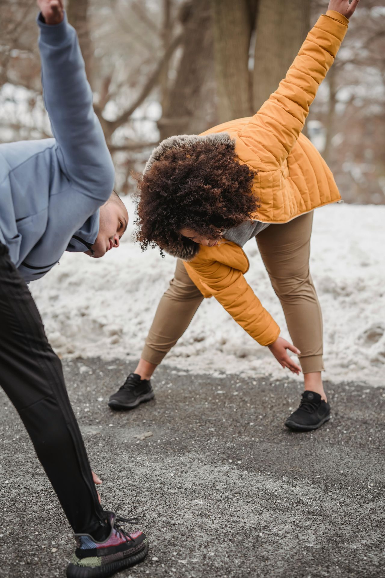 cis gendered black couple standing on pavement both reaching out stretching and touching their toes