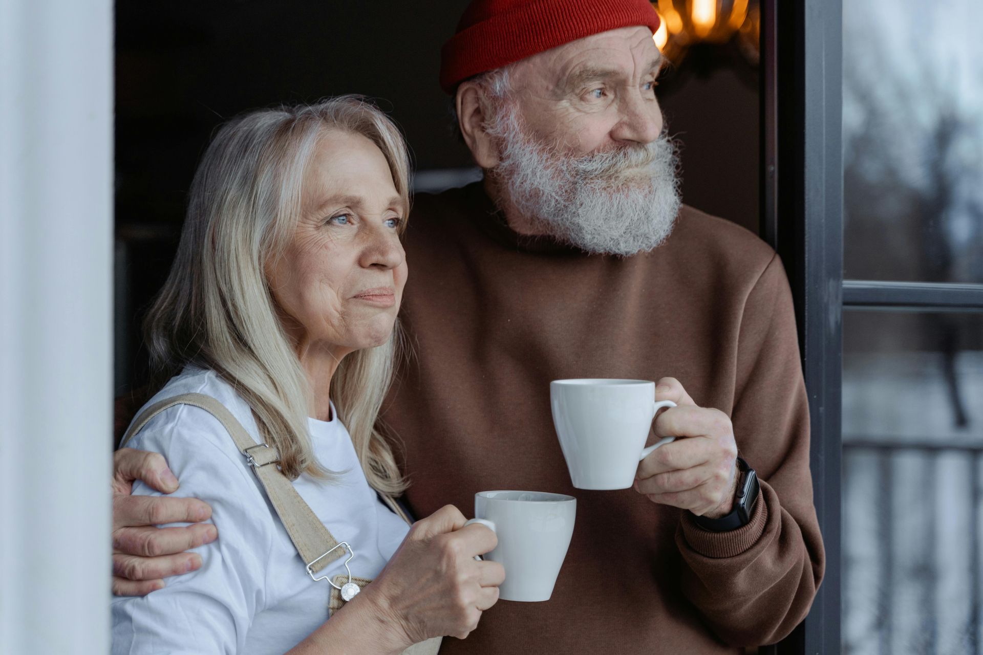 mixed gender older couple looking out a window together both enjoying a cup of coffee and softly smiling