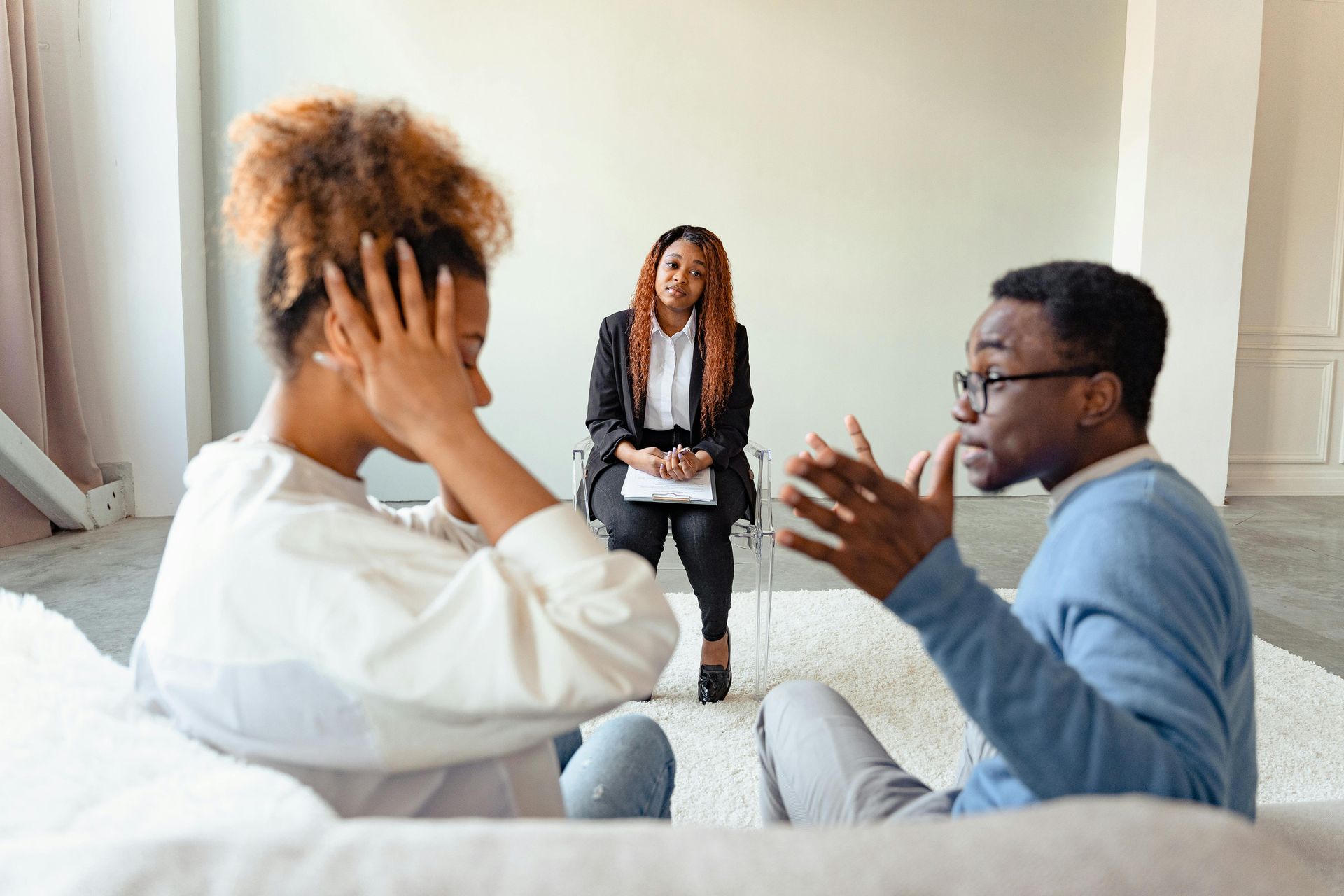 cis gender male female couple in therapy session, therapist in the background, the female partner has her ears covered and the male partner is yelling