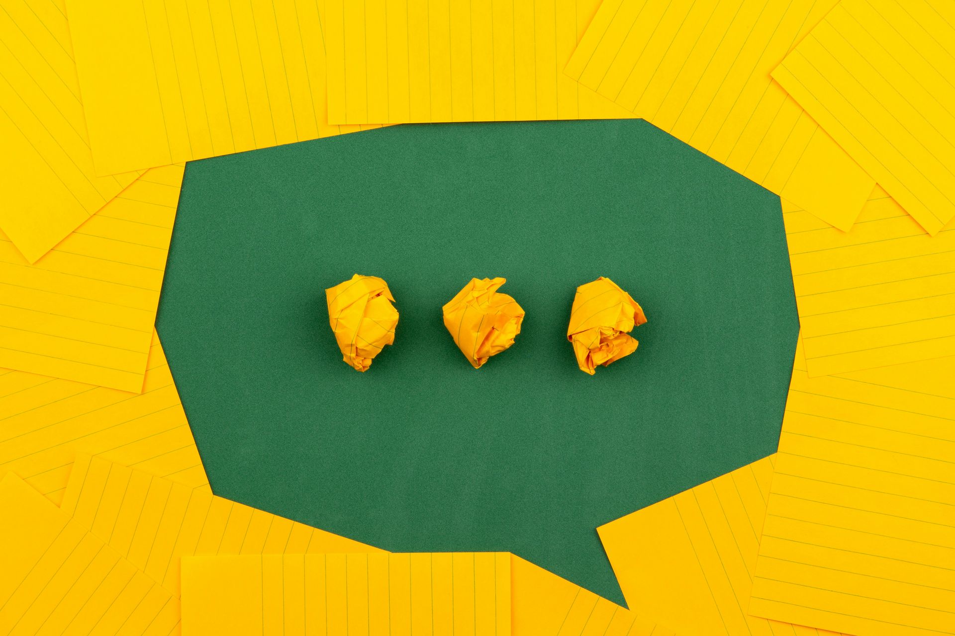 3 yellow balled up pieces of paper in the middle of a green speech bubble on a yellow background