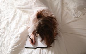A woman laying in her bed journaling about her life. Represents the need for self-awareness therapy in Katy, TX 77494