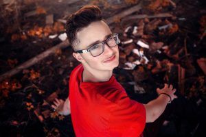 A teenage boy sitting on leaves and looking up at another person that he admires. He has learned from mature adults in his life as well as from attending teen therapy in Katy, TX 77494