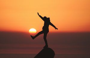 A person standing on a cliff at sunset exploring self care. Represents the need for self-care check and therapy in Katy, TX 77494