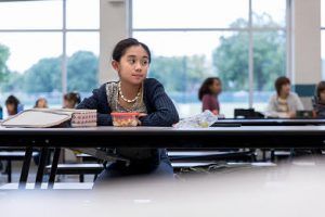 Lonely schoolgirl looks to the side while eating by herself in the school cafeteria. Other students are eating together in the background. Girl sitting at a lunch table during school. Early signs for autism in children can include delayed milestones, limited social interactions with peers, and repetitive actions or fixations. Early signs of Autism blog. Therapy in Katy Texas. Counseling Center at Cinco Ranch.