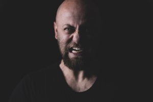 A man with an angry face showing aggression. He is being taught through men's therapy in Katy, TX 77494 that he can be assertive to get his needs met.