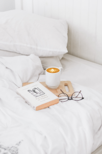 A book and cup of coffee on a bed that represents the need to handle stress and maintain self-care. 