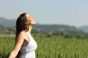 A teen girl holding her arms out soaking up sunlight while standing in the grass with her eyes closed. She is experiencing happiness after attending teen group therapy in Katy, TX 77494 and working through issues such as anxiety
