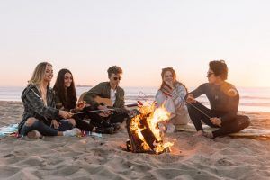 Young adults sitting around a campfire at the beach learning how to spend time being free. Represents the need for counseling fro perfectionism in Katy, TX