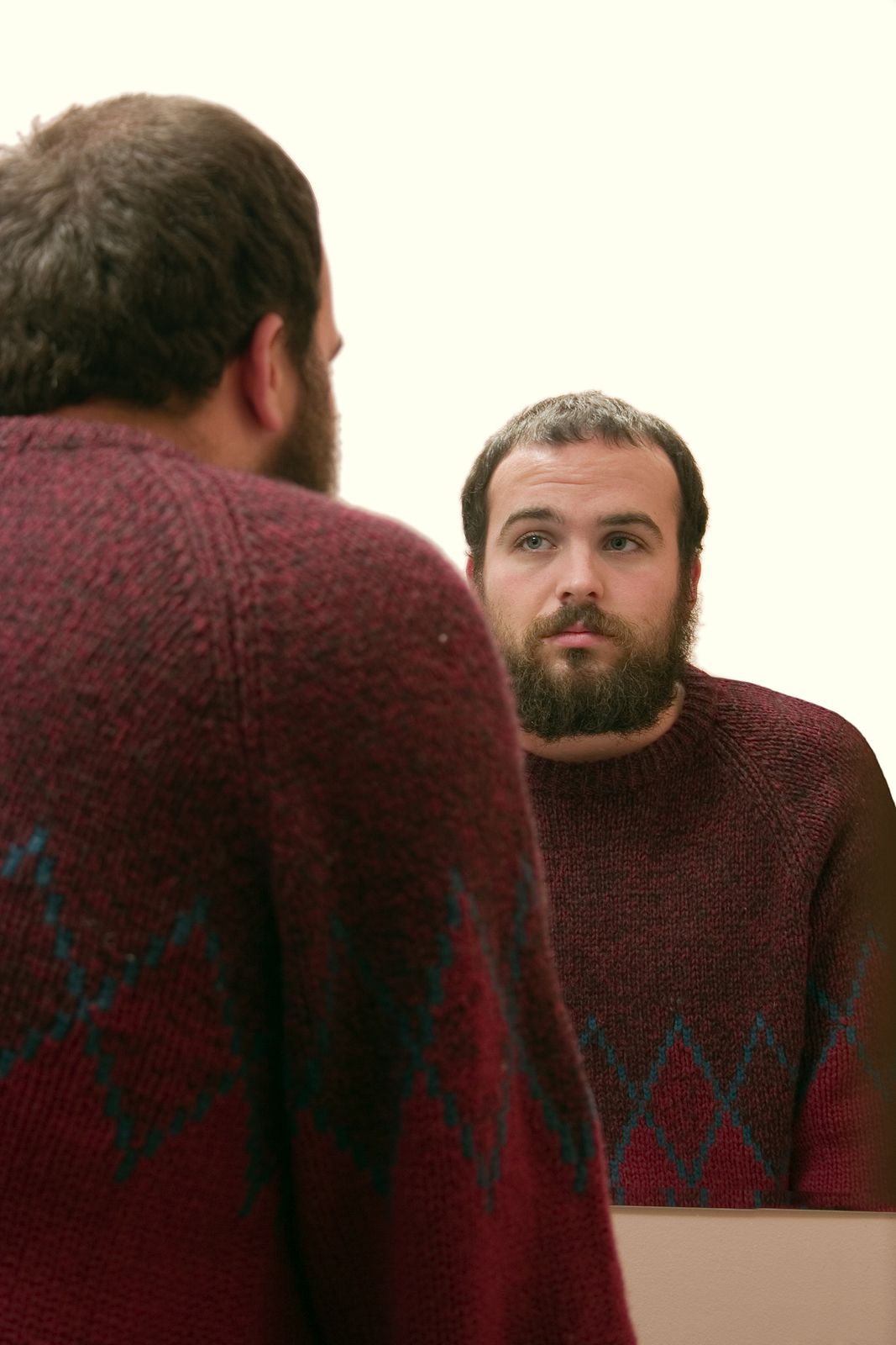 A man studies his reflection in the mirror with a thoughtful, uncertain expression, capturing the quiet self-scrutiny common with body image issues in Palm Beach County, FL. A body image counselor in Delray Beach, FL can help him explore these feelings through EMDR therapy in Palm Beach County, FL."