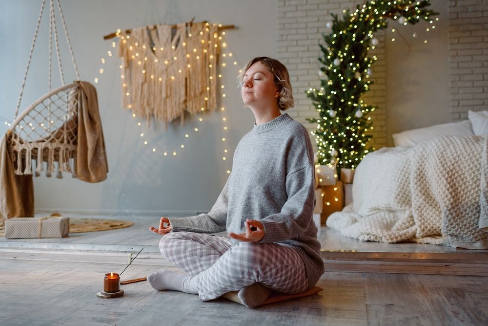 A person meditates on the floor in a warm, softly lit holiday environment, practicing grounding techniques that support emotional regulation. This peaceful scene mirrors strategies often encouraged in addiction counseling in Delray Beach, FL or sessions with an addiction therapist in Palm Beach, FL. Many individuals working through different types of addiction in Palm Beach, FL use mindfulness to navigate seasonal triggers.
