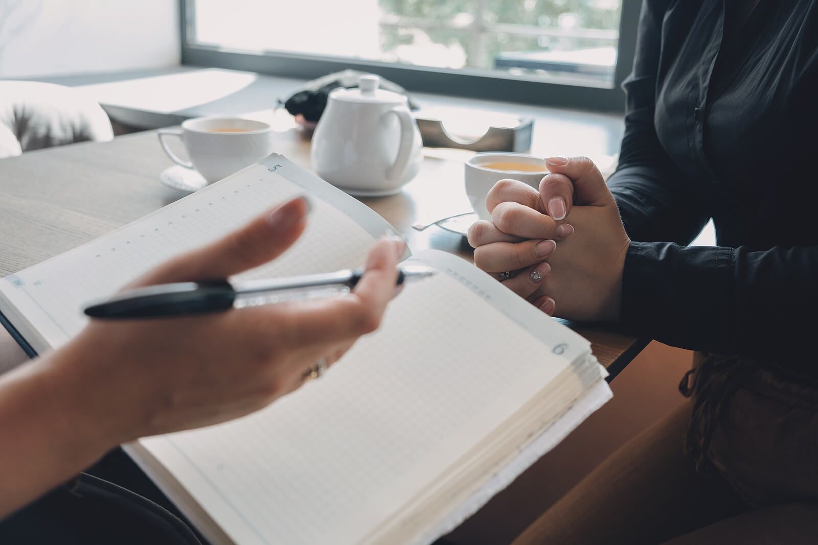 Therapist’s hands holding a planner while speaking with a client at a table, symbolizing a structured treatment plan and supportive care. This relates to emdr therapy in palm beach county, fl, working with an emdr therapist in miami, fl, and finding an emdr therapist in palm beach county, fl for trauma and chronic pain support.