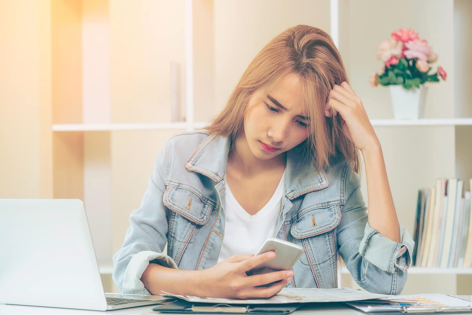 A young woman sits at her desk looking anxiously at her phone, hand pressed to her head — capturing the kind of everyday trigger that can set off an emotional flashback in those living with CPTSD. A complex PTSD therapist in Palm Beach County, FL can help you understand why small moments like a delayed text can feel so overwhelming. With the right complex PTSD treatment in Palm Beach County, FL, those reactions can finally begin to make sense and shift.