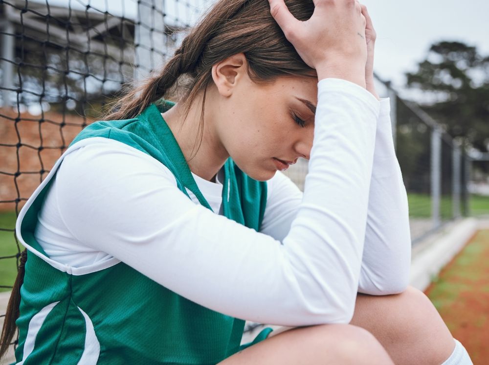 Young female athlete in a green jersey sitting by the net with her head in her hands, illustrating how emdr therapy in palm beach county, fl and emdr intensives in palm beach county, fl with an emdr therapist in palm beach county, fl can help with performance anxiety.