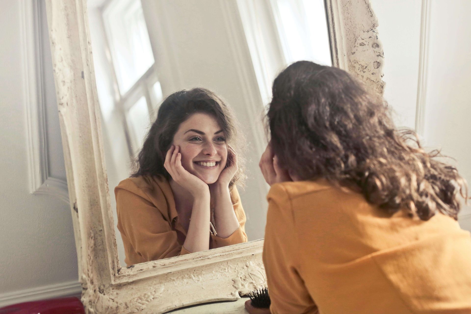 Woman smiling at her reflection after healing through trauma treatment in Palm Beach County, FL with a trauma therapist in Delray Beach, FL providing trauma therapy in Delray Beach, FL for individuals learning that over responsibility is a trauma response.