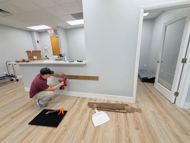 A team member crouches down in the new office space, using a power drill to install wood paneling along the base of the reception desk while new flooring gleams in the background. This image captures the hands-on build-out process that the Mangrove Therapy Group team undertook to create a space that truly reflects their commitment to quality care as a leading therapist in Delray Beach, FL. Every wood panel, brick, and soundproofed wall was installed with the intention of making clients feel safe, comfortable, and ready to engage in EMDR therapy in Delray Beach, FL.
